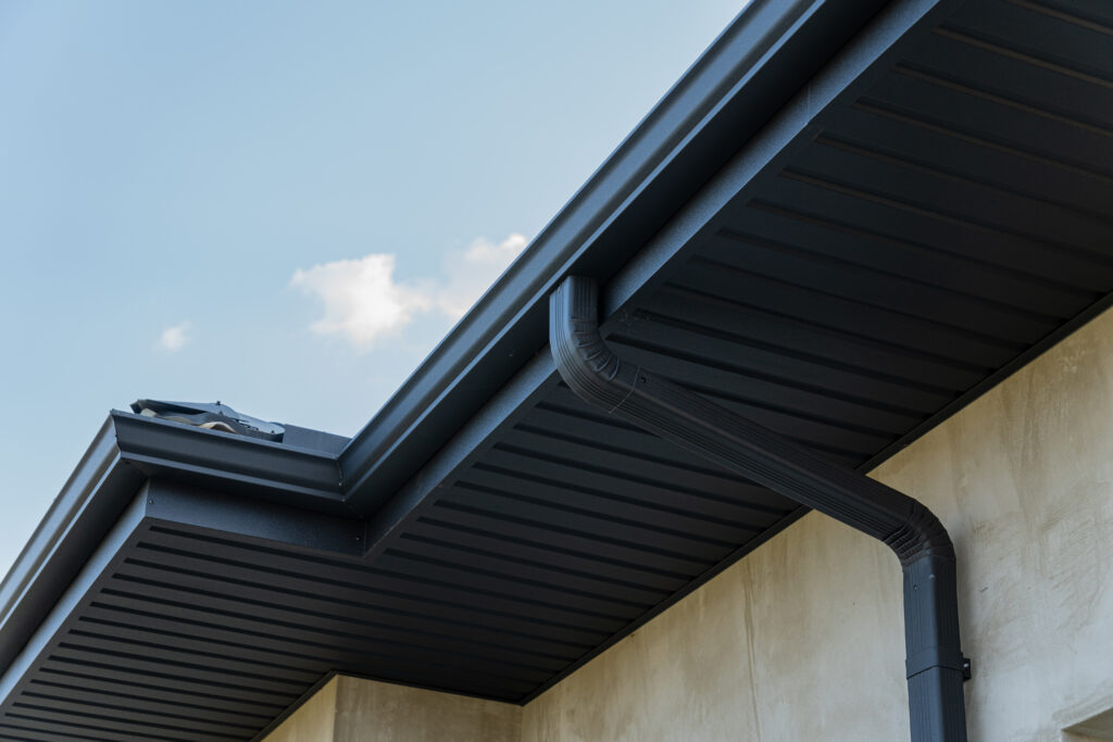 Close view of a roof edge and downspout against a bright blue sky highlights contemporary construction features and materials.