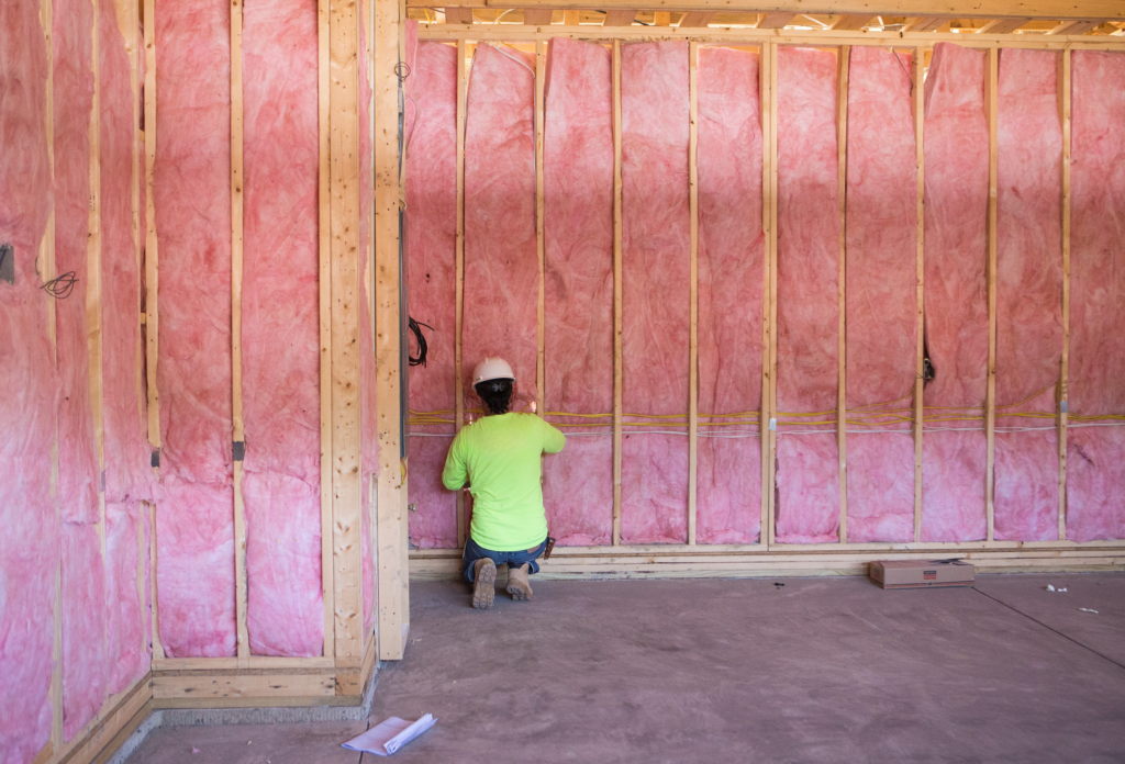 An insulation contractor installing fiberglass batt insulation into a wall