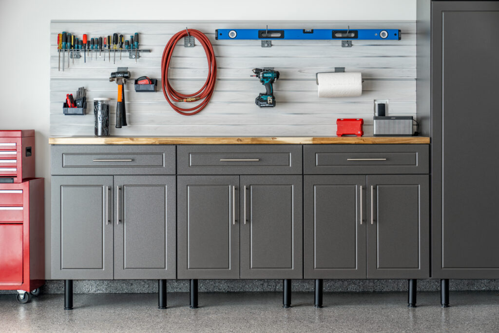 Custom grey garage storage cabinets with a wood workbench top and slatwall tool organization, situated on a seamless polyurea concrete floor coating with a full flake finish.